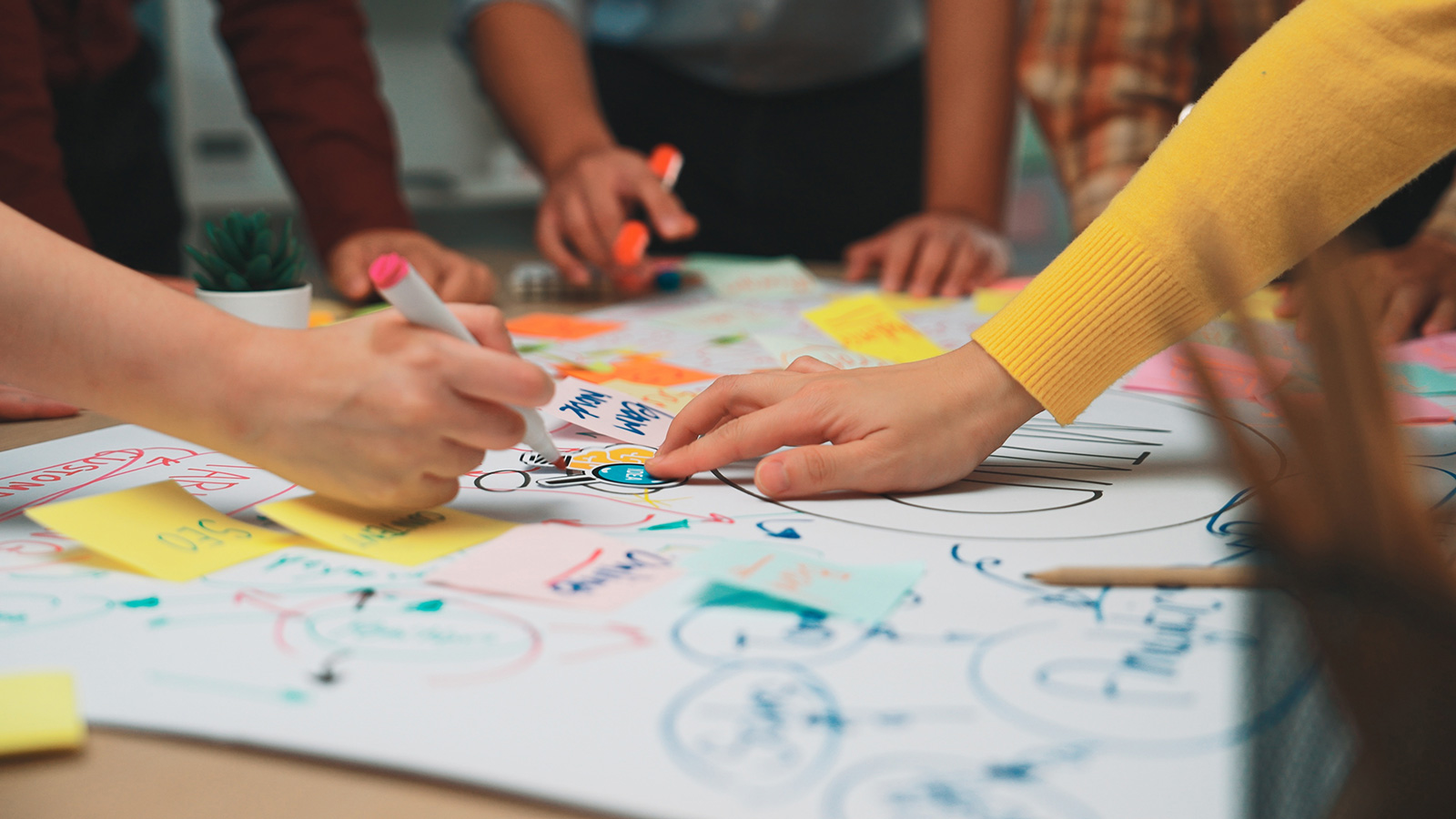 Team members collaborating around a table covered with sticky notes and diagrams during a brainstorming workshop.